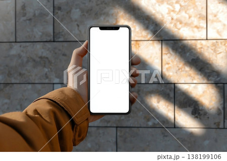 Man holding smartphone mobile device mockup template in an urban outdoor environment with sharp sunlit shadows. Isolated surface to place your design. 138199106