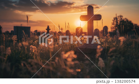 Peaceful cemetery scene at sunset, featuring a stone cross surrounded by wild grass, with the sun setting beautifully in the background and other tombstones visible. 138200574