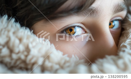 Young person's eyes, wrapped in a blanket, showing deep, soulful amber eyes that convey curiosity and depth. 138200595