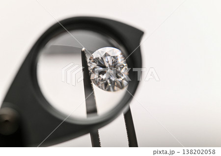 Diamond viewed through a magnifying glass held by tweezers 138202058