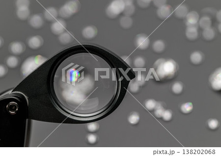 Magnifying glass highlights detailed facets of diamond-like stones against soft Magnifying glass highlights detailed facets of diamond-like stones against soft 138202068