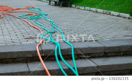 Long turquoise and orange garden hoses sprawled across a stone tile path next to a green lawn Long turquoise and orange garden hoses sprawled across a stone tile path next to a green lawn 138202135