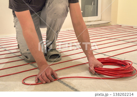 Electrician installing heating red electrical cable wire on cement floor in unfinished room. Renovation and construction, comfortable warm home concept. 138202214