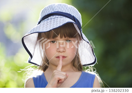 Close-up portrait of serious little girl in a big hat. Child having fun time outdoors in summer. Close-up portrait of serious little girl in a big hat. Child having fun time outdoors in summer. 138202330
