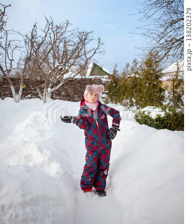 Smiling girl winter clothes holding large snowball standing in deep snow near house wooden fence 138202379