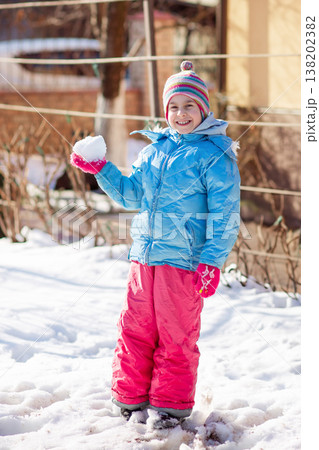 Smiling child colorful winter clothes standing on snow with trees and houses in sunny background Smiling child colorful winter clothes standing on snow with trees and houses in sunny background 138202382