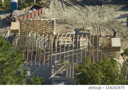 Builders working on roof construction of unfinished residential house with wooden frame structure in Florida suburban area. Housing development concept 138202675