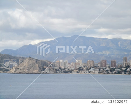 Scattered towers over rocky shoreline under cloudy sky with contrasting natural and urban elements 138202975