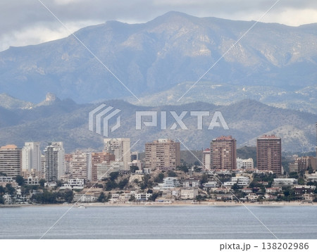 Energetic coastal neighborhood featuring midlevel towers and busy promenade with mountain landscape beyond Energetic coastal neighborhood featuring midlevel towers and busy promenade with mountain landscape beyond 138202986