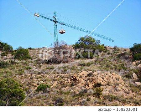 Gondola transports supplies, Aerial crane moves cargo across rocky hillside landscape under blue sky 138203081