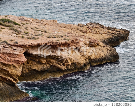 Scenic rocky overhang beside ocean showcasing erosion and weathering patterns under warm sunlight Scenic rocky overhang beside ocean showcasing erosion and weathering patterns under warm sunlight 138203086