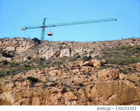 Crane hoists load over ridge, Heavy machinery raises cargo over rocky landscape under open sky 138203103
