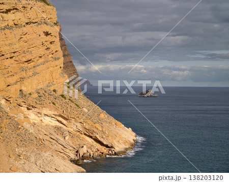 Dusky sandstone outcrop meets vast sea, Gloomy formations against turbulent waters under heavy skies 138203120