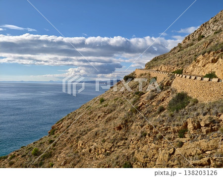 Cliff path adventure, Scenic trail above turquoise waters with distant clouds and sparse flora Cliff path adventure, Scenic trail above turquoise waters with distant clouds and sparse flora 138203126