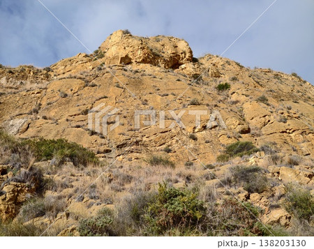 Illuminated summit with limited shrubbery and sharp cliffs beneath overcast sky creates solitude 138203130