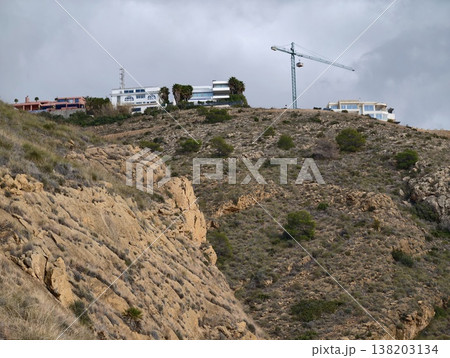 Industrial construction scene, Urban development activity against rugged hillside under cloudy sky 138203134