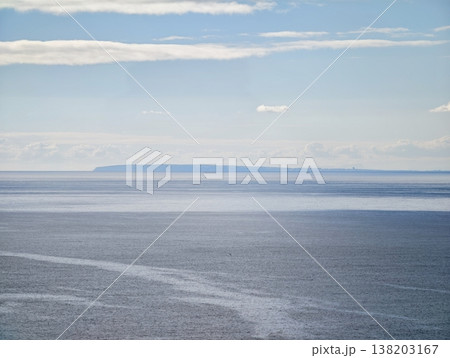 Serene scene depicting layered cloud formations over placid sea with subtle pastel hues and distant landmasses 138203167