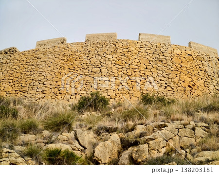 Sundrenched round stone wall with lush grass foreground showcasing weathered craftsmanship Sundrenched round stone wall with lush grass foreground showcasing weathered craftsmanship 138203181