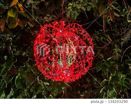 Vivid red globe hangs amidst lush green ivy with detailed wirework and dramatic lighting effects 138203290