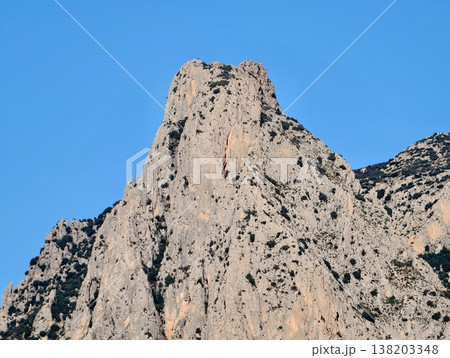 Sunlit rocks with dramatic features, Vertical limestone formation with sharp edges under clear sky scene 138203348