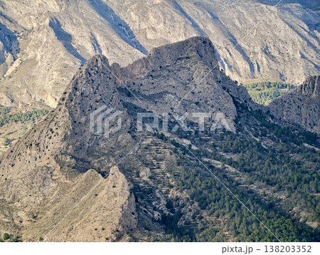 Rugged peak with scenic views, Jagged mountain rise highlighted by sunlight above verdant landscape 138203352