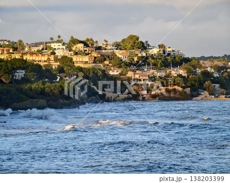 Lush cliffs with ocean views, Sunlit dwellings nestled among greenery overlooking lively rolling surf 138203399