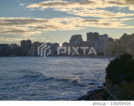 Sunset skyline over turbulent waters, Dusk over ocean revealing shimmering clouds and distant buildings Sunset skyline over turbulent waters, Dusk over ocean revealing shimmering clouds and distant buildings 138203416