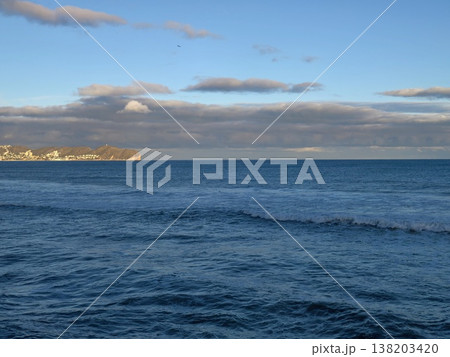 Serene ocean view displaying distant harbor town silhouette with soft lighting and peaceful community ambiance 138203420