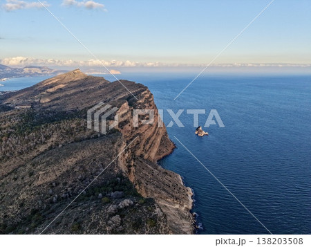 Steep cliff side with lone vessel floating nearby, Towering cliff with solitary boat amidst tranquil waters Steep cliff side with lone vessel floating nearby, Towering cliff with solitary boat amidst tranquil waters 138203508
