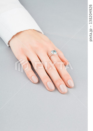 Beautiful female hand with gold ring with diamonds and aquamarine on gray background Beautiful female hand with gold ring with diamonds and aquamarine on gray background 138204926
