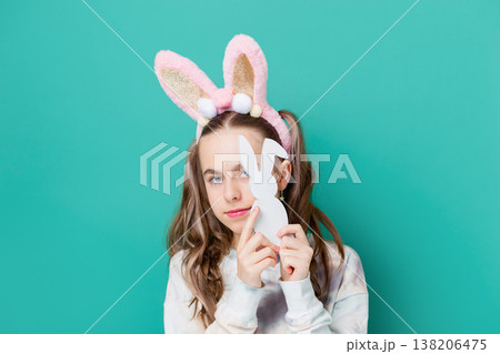 Teenage girl with bunny ears holding wooden bunny toys smiling on bright green background studio Teenage girl with bunny ears holding wooden bunny toys smiling on bright green background studio 138206475