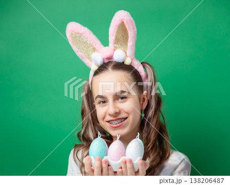 Teenage girl with bunny ears holding pastel Easter eggs in egg holder on green studio background Teenage girl with bunny ears holding pastel Easter eggs in egg holder on green studio background 138206487
