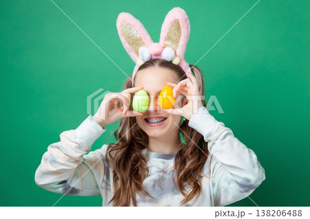 Teenage girl with bunny ears holding pastel Easter eggs in egg holder on green studio background 138206488