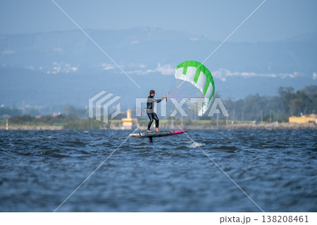A middle-aged man in a wetsuit glides on a hydrofoil board with a green and white kite A middle-aged man in a wetsuit glides on a hydrofoil board with a green and white kite 138208461