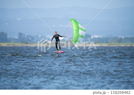 A middle-aged man in a wetsuit glides on a hydrofoil board with a green and white kite 138208462