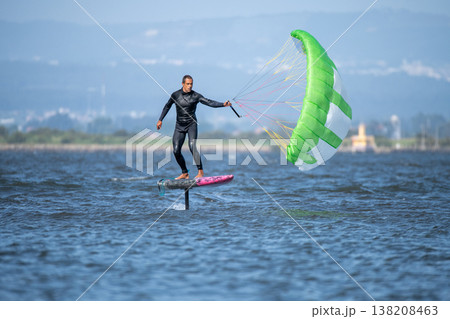A middle-aged man in a wetsuit glides on a hydrofoil board with a green and white kite 138208463