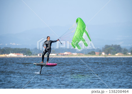 A middle-aged man in a wetsuit glides on a hydrofoil board with a green and white kite 138208464