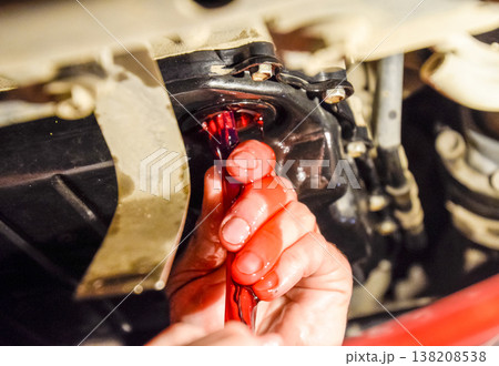 Oil change in automatic transmission. Filling the oil through the hose. Car maintenance station. Red gear oil. The hands of the car mechanic in oil Oil change in automatic transmission. Filling the oil through the hose. Car maintenance station. Red gear oil. The hands of the car mechanic in oil 138208538