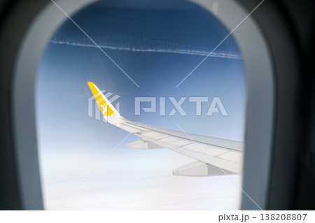 Flying airplane over the clouds. Airplane wing against a clear blue sky background during a commercial flight, conceptual travel and transportation photography. Flying airplane over the clouds. Airplane wing against a clear blue sky background during a commercial flight, conceptual travel and transportation photography. 138208807