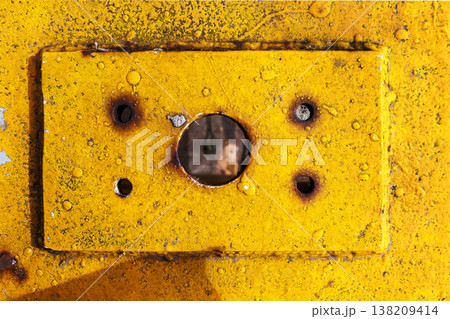 Yellow painted metal plate with a central screw hole and rust stains, showing weathered industrial surface texture. grunge background Yellow painted metal plate with a central screw hole and rust stains, showing weathered industrial surface texture. grunge background 138209414