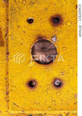 Yellow painted metal plate with a central screw hole and rust stains, showing weathered industrial surface texture. grunge background 138209415