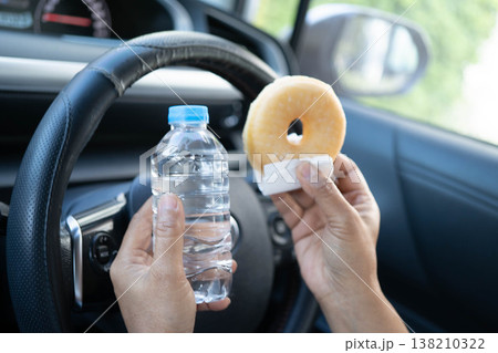 Asian woman driver hold and eat hamburger in car, dangerous and risk an accident. Asian woman driver hold and eat hamburger in car, dangerous and risk an accident. 138210322
