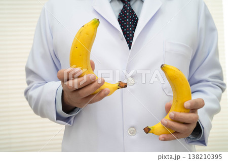 Male doctor stands holding a banana, penis health. 138210395