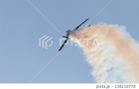 Aerobatic propeller airplane performing a steep maneuver while releasing a trail of smoke across a clear blue sky. 138210778