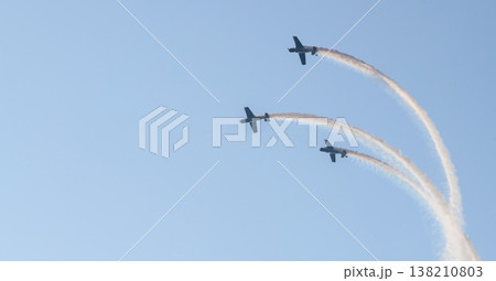 Three aerobatic aircraft performing a synchronized aerial maneuver with curved smoke trails against a clear blue sky during an aviation airshow. Dynamic formation display in an open sky background 138210803