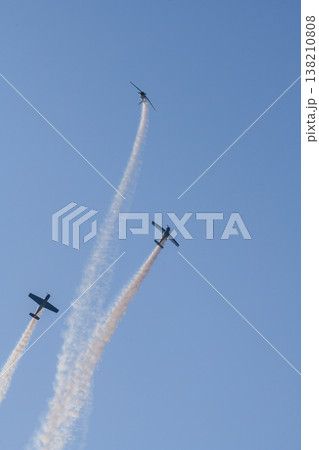 Three aerobatic propeller airplanes performing a synchronized aerial maneuver with sweeping smoke trails across a clear blue sky during a dynamic aviation display 138210808