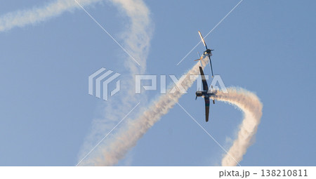 Two aircraft performing aerobatic maneuvers with smoke trails against a clear sky during an aerial aviation display Two aircraft performing aerobatic maneuvers with smoke trails against a clear sky during an aerial aviation display 138210811
