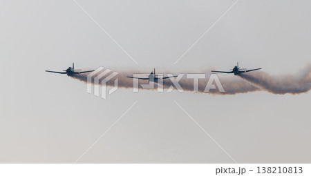 Three propeller aircraft perform a synchronized formation flight releasing smoke trails against a clear sky during an aerial display at an aviation event 138210813