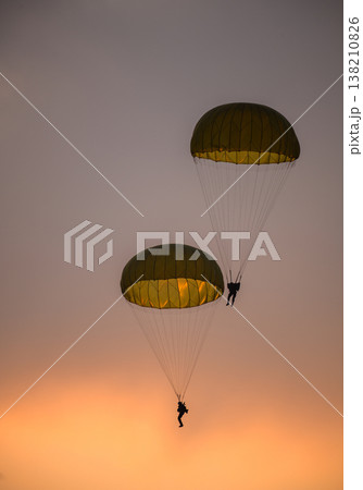 Two combat paratroopers deploying by parachute during an air show demonstration. Silhouettes of troopers descending with glowing parachute canopies against a sunset sky Two combat paratroopers deploying by parachute during an air show demonstration. Silhouettes of troopers descending with glowing parachute canopies against a sunset sky 138210826