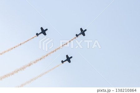 Three aerobatic aircraft performing a synchronized aerial maneuver with curved smoke trails against a clear blue sky during an aviation airshow. Dynamic formation display in an open sky background Three aerobatic aircraft performing a synchronized aerial maneuver with curved smoke trails against a clear blue sky during an aviation airshow. Dynamic formation display in an open sky background 138210864